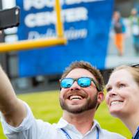 Two guests taking a selfie on the field at the Jamie Hosford Football Center dedication.